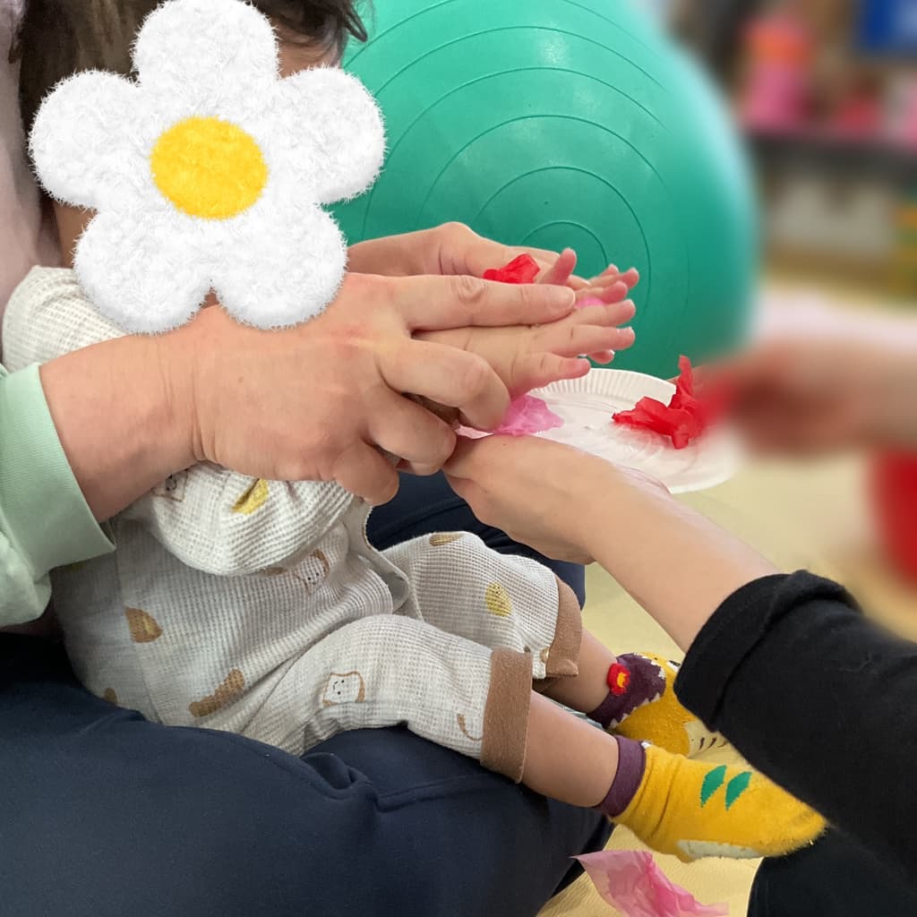子どもが白い台紙に赤やピンクの花紙を貼って母の日の工作に取り組んでいる様子