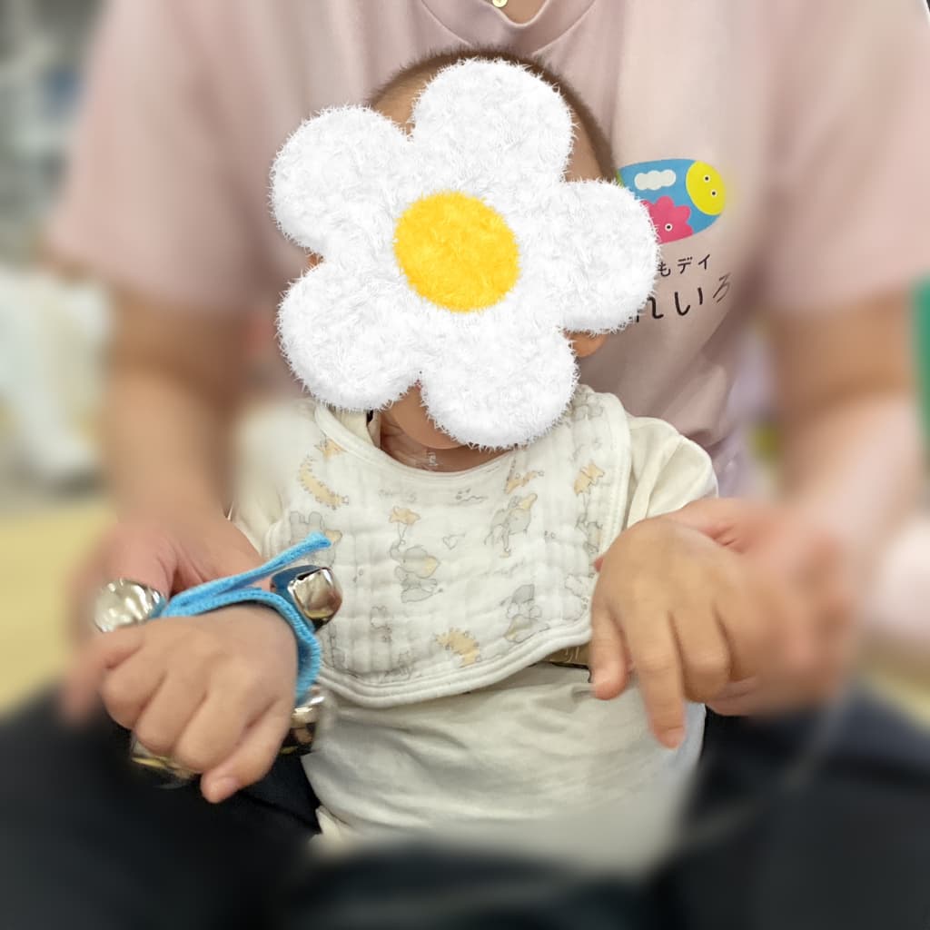 大人の膝の上に座った子どもが、手首につけた鈴を前に出している様子