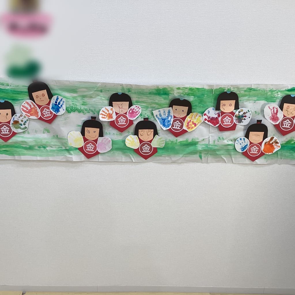 子どもたちの手形で手が作られている金太郎の壁面飾り。9人分の金太郎が横並びに並んでいる。