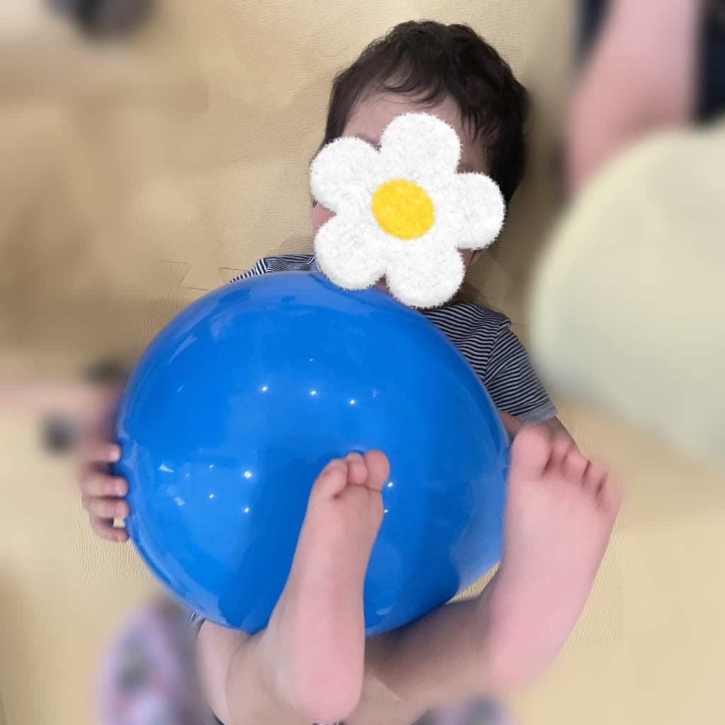床に寝転んだ子どもが、大きな青い風船を両手と足で抱えるように持っている様子