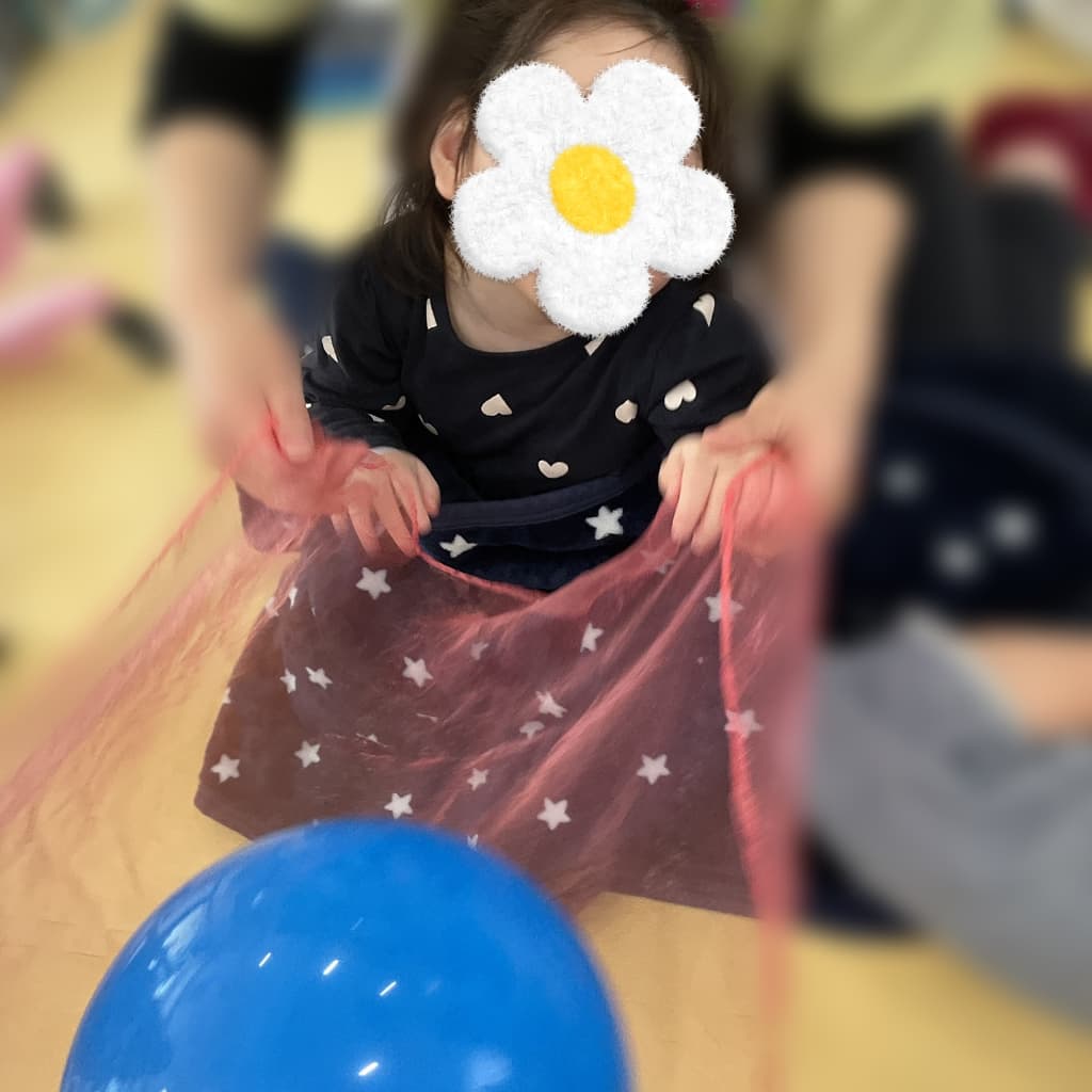 子どもが赤い星柄の薄布を両手で持ち、その上に青い風船が置かれている様子
