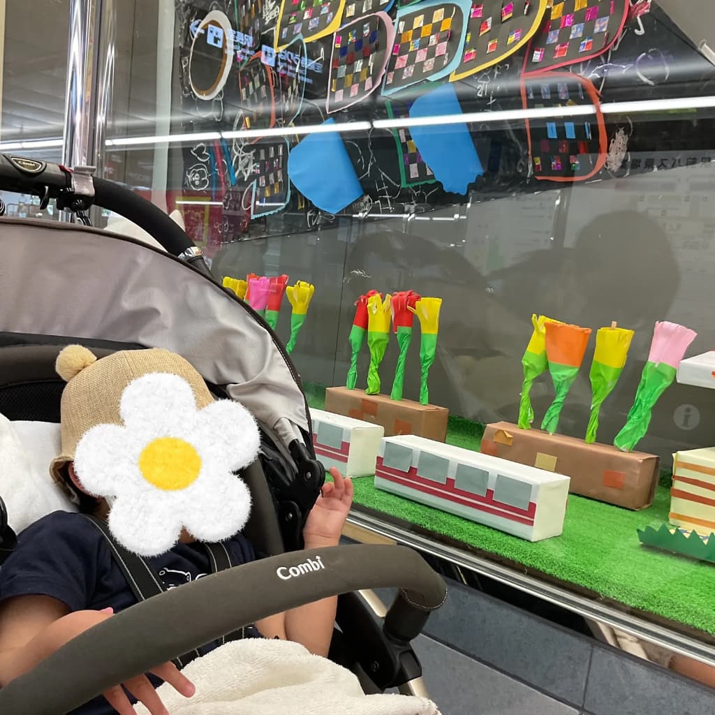 ベビーカーに乗った子どもが、壁に貼られたこいのぼりやお花の制作を眺めている
