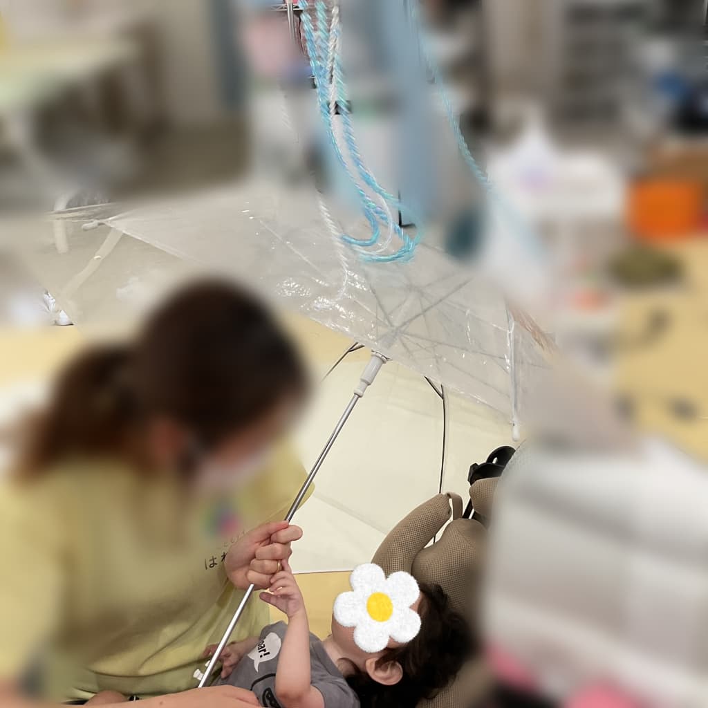 支援者と向かい合った子どもが透明なビニール傘の柄を一緒に持ち、傘の大きさや手触りを感じながら遊んでいる様子