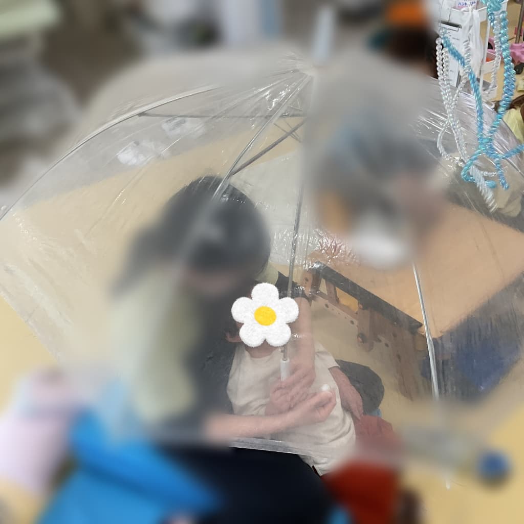 透明なビニール傘の内側に、支援者と一緒に座る子どもの姿がぼんやりと見えている様子