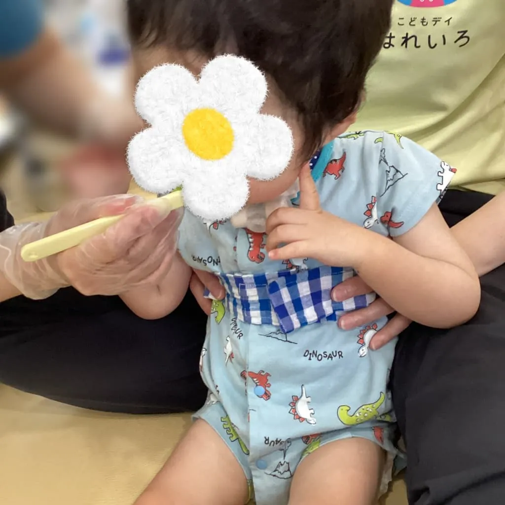 大人に脇を支えられた子どもが、黄色い歯ブラシで歯磨きをしてもらっている