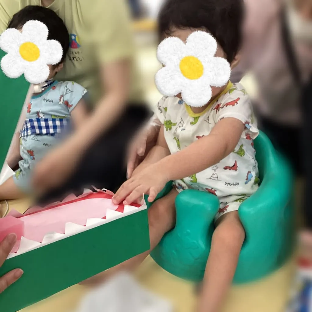 バンボに座った子どもが、紙でできたワニの模型の歯を触っている