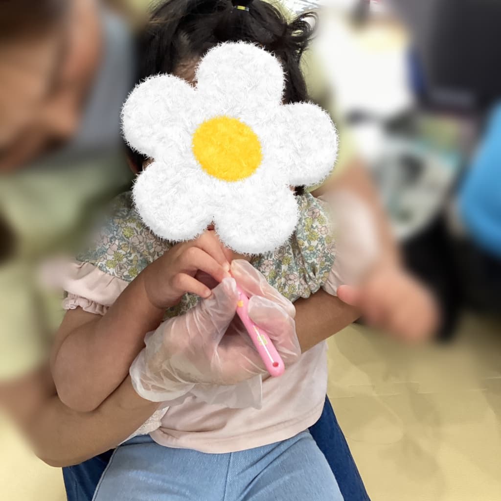 支援者に身体を支えられた子どもが、ピンク色のおもちゃの歯ブラシを手に持ち、歯みがきしている様子