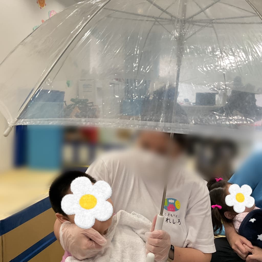 支援者が透明なビニール傘を指しながら、子どもを抱っこしている様子