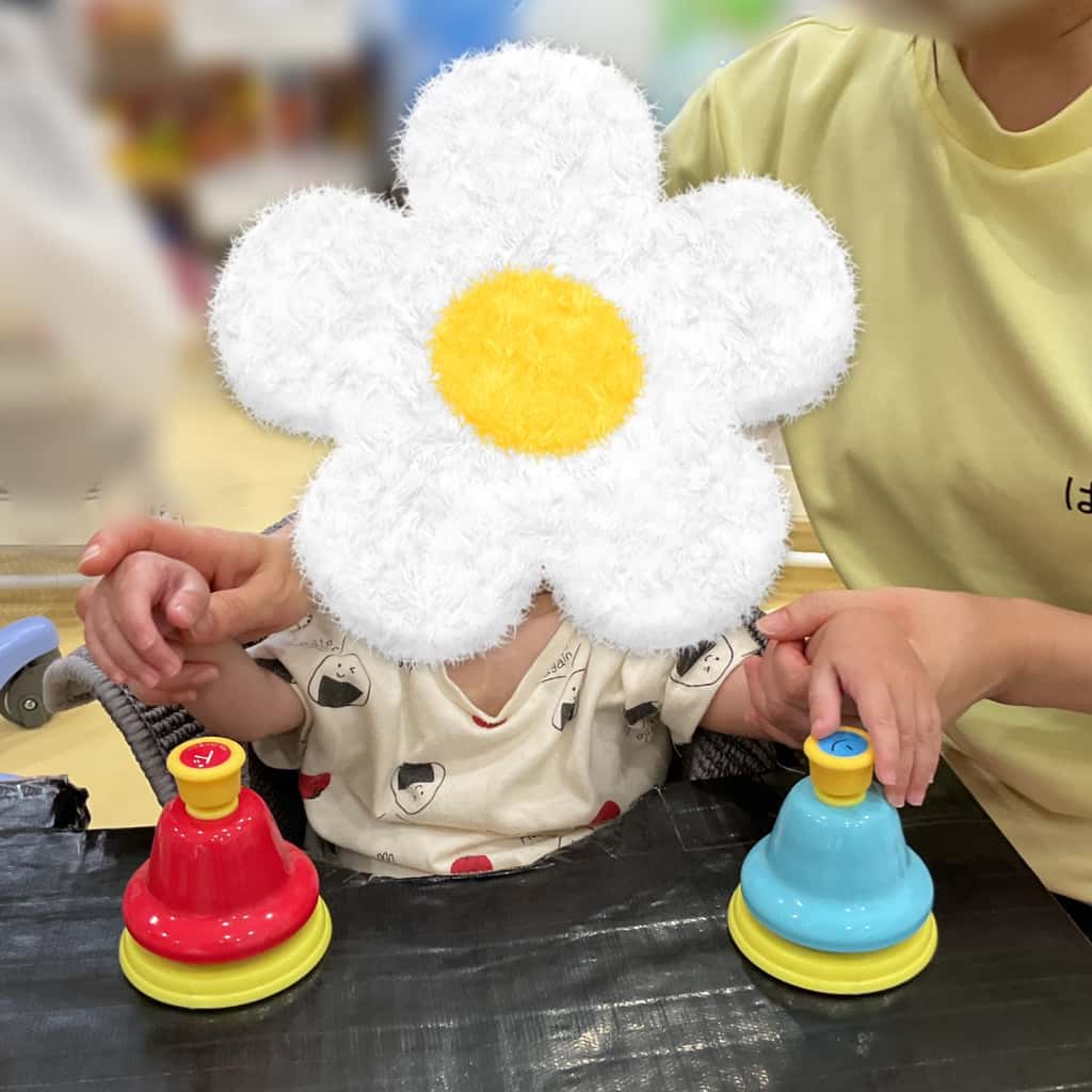 子どもが支援者と一緒に赤と青のベルを鳴らす活動に取り組んでいる様子
