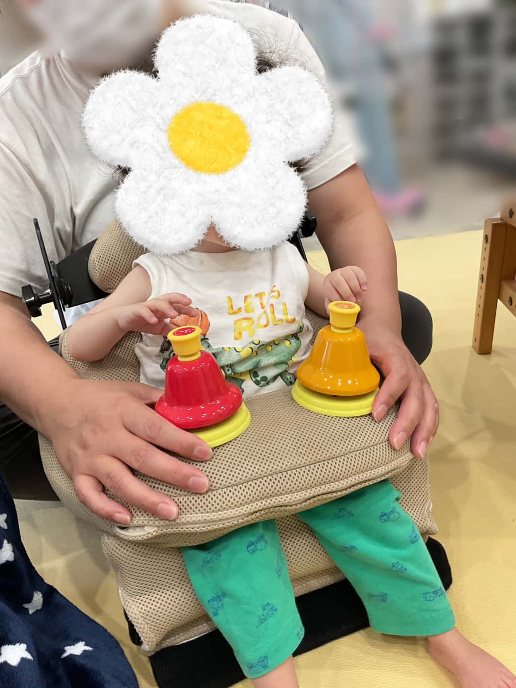 座位保持椅子に座った子どもが両手でベルに触れながら音遊びを楽しんでいる様子