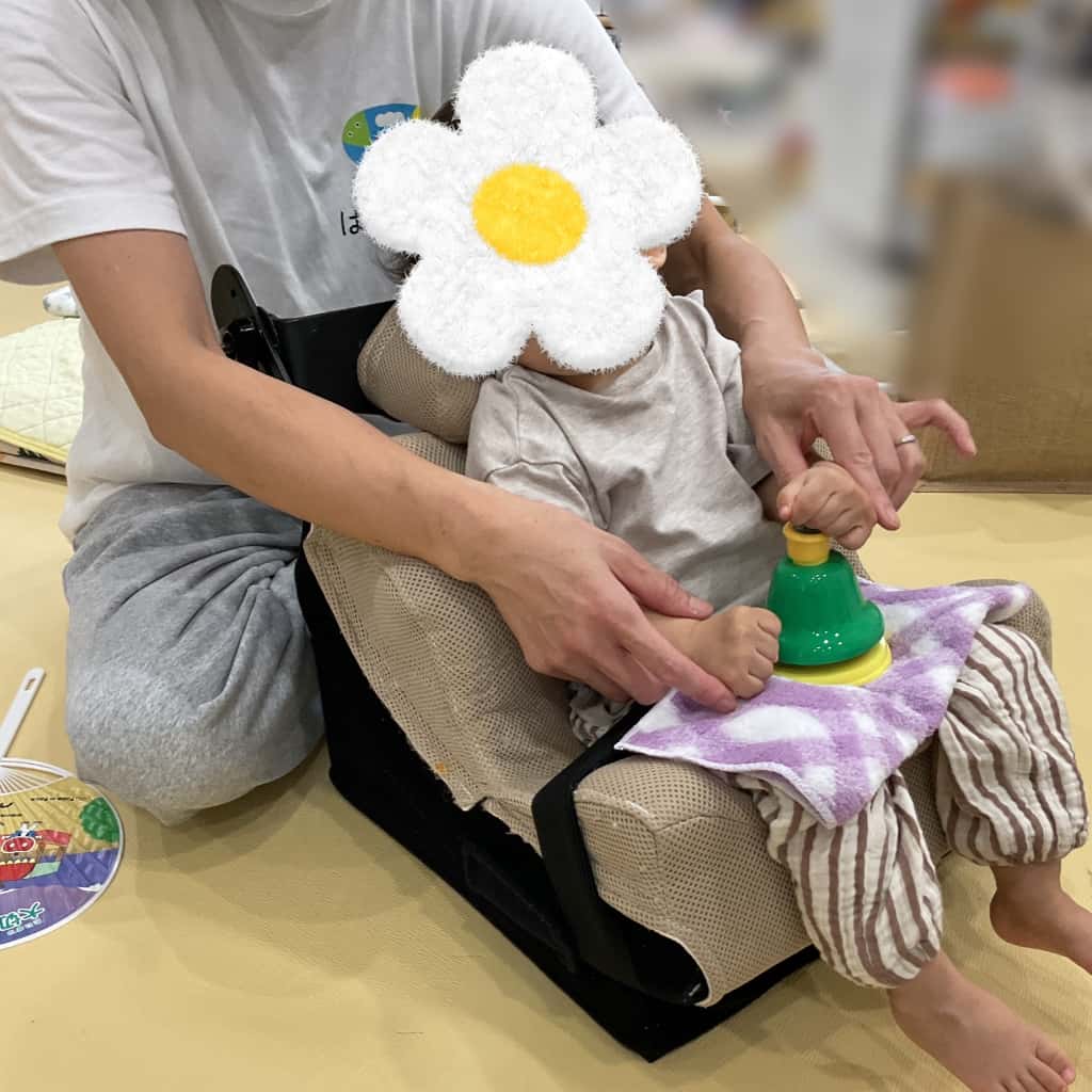 座位保持椅子に座った子どもが支援者と一緒にハンドベルを鳴らす活動をしている様子