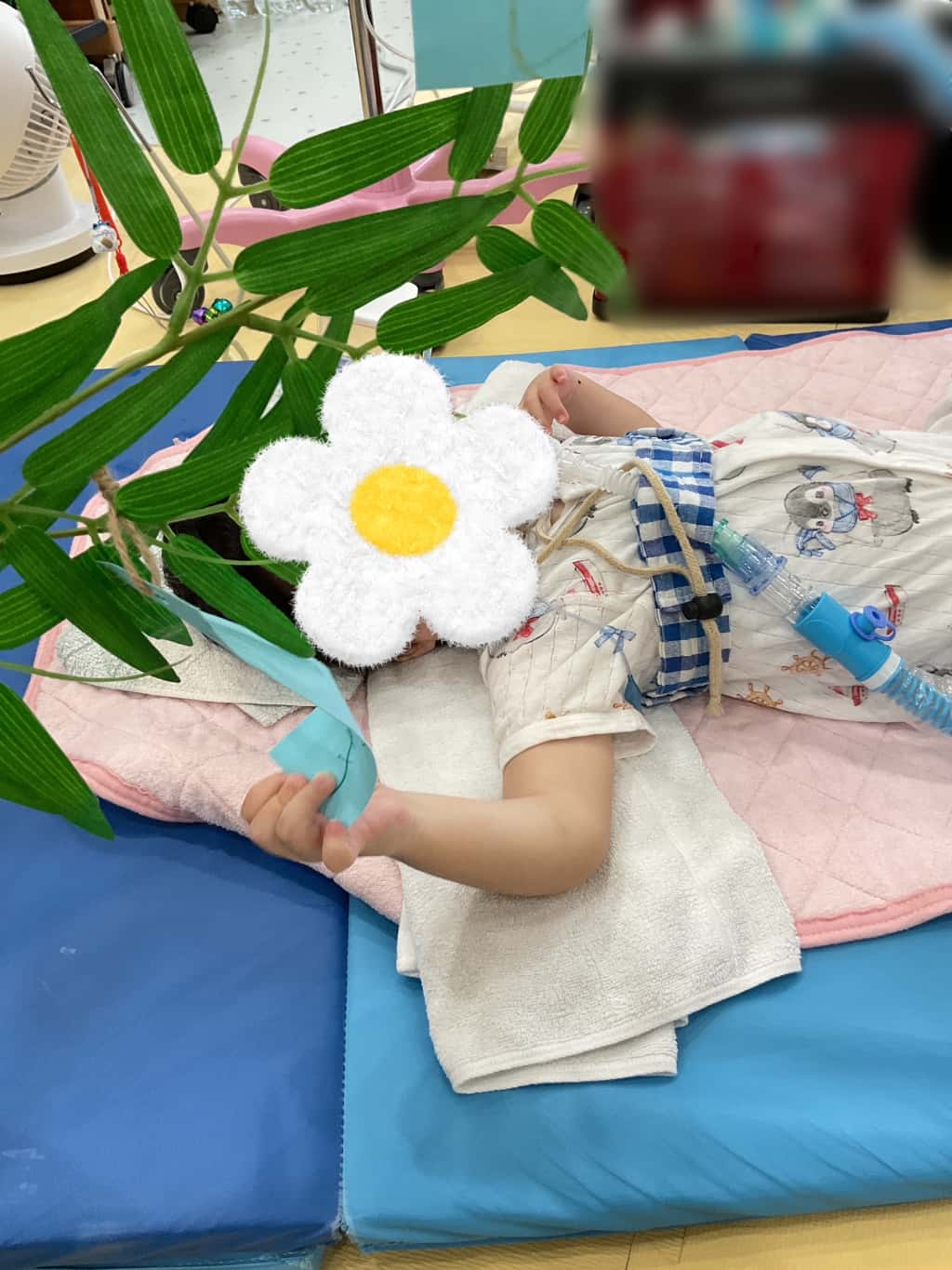 人工呼吸器を装着して横になっている子どもが手を伸ばして、七夕の短冊を手に持って笹に飾ろうとしている様子