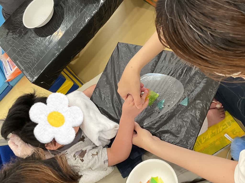 椅子に座って、作業台の上で支援者に手を添えてもらいながら制作している子ども