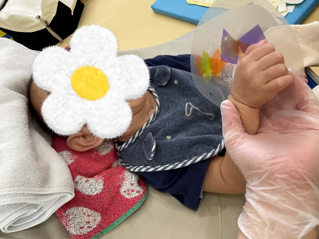 仰向けになった状態で、支援者に手を添えてもらい制作をしている子ども。透明な丸いビニール台紙にカラフルなセロハンを張り付けている