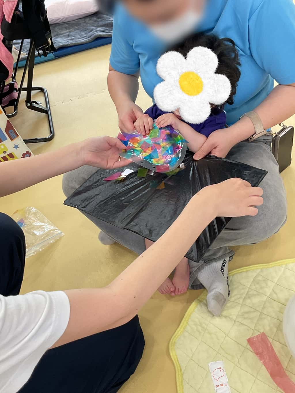 支援者の膝の上に座り、ビニールの方の上にカラフルなセロハンを貼って制作をしている子ども