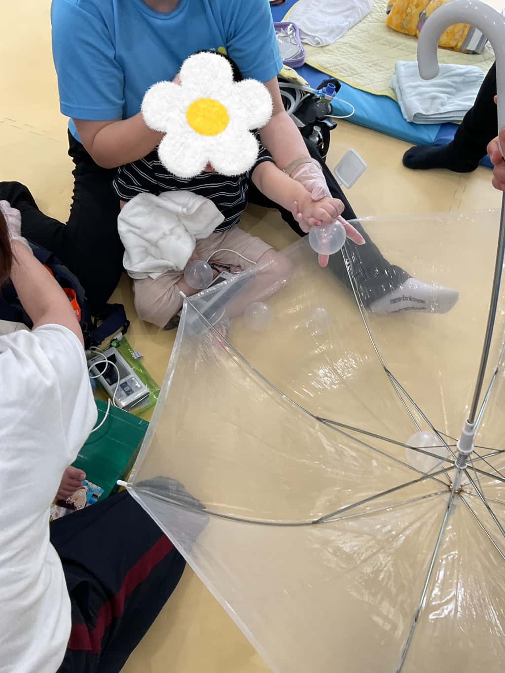 大人の膝の上に座った子どもが、逆さにした透明な傘の中に、風船ボールを入れようと手を伸ばして遊んでいる様子