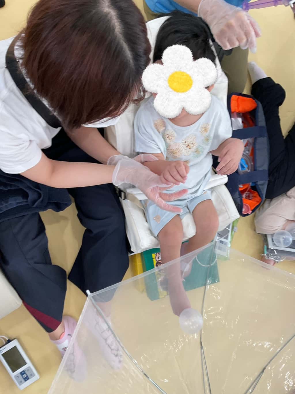 クッションチェアに座った子どもが、大人と一緒に透明な傘の中の風船ボールに触れて遊んでいる様子