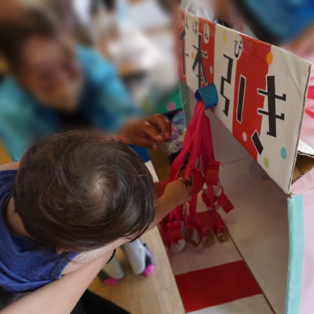 赤いひもと景品が吊り下げられた箱の中に、子どもが手を伸ばしてひもを選んでいる