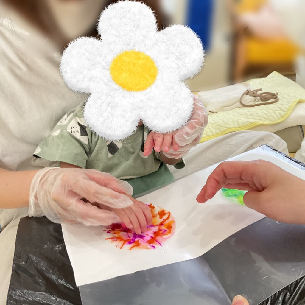 室内でスタッフに手を支えてもらいながら、絵の具を使ったフィンガーペイントを楽しむ子ども