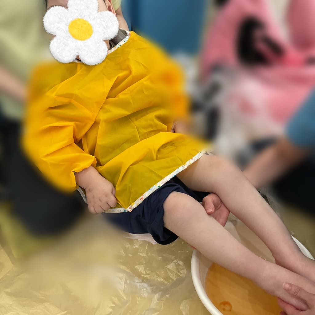 室内でスタッフに身体を支えてもらいながら、足を色水につける子ども