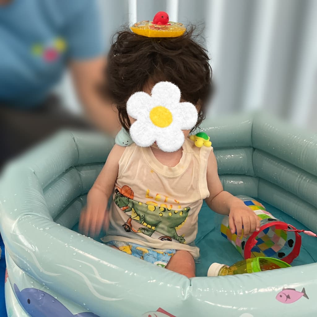 水遊び用のおもちゃを頭に載せ、室内プールに座る子ども