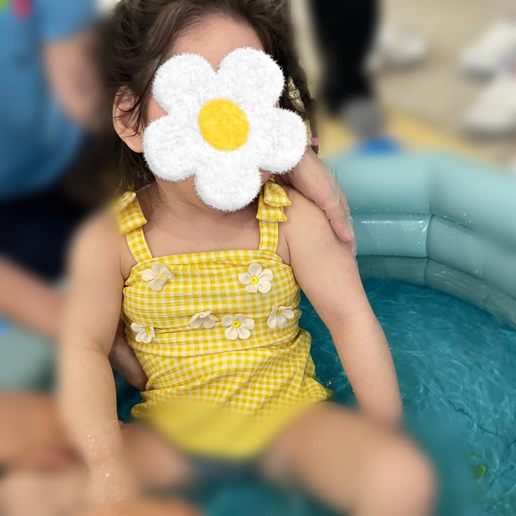 黄色いチェック柄の水着を着て、室内のビニールプールに座る女の子