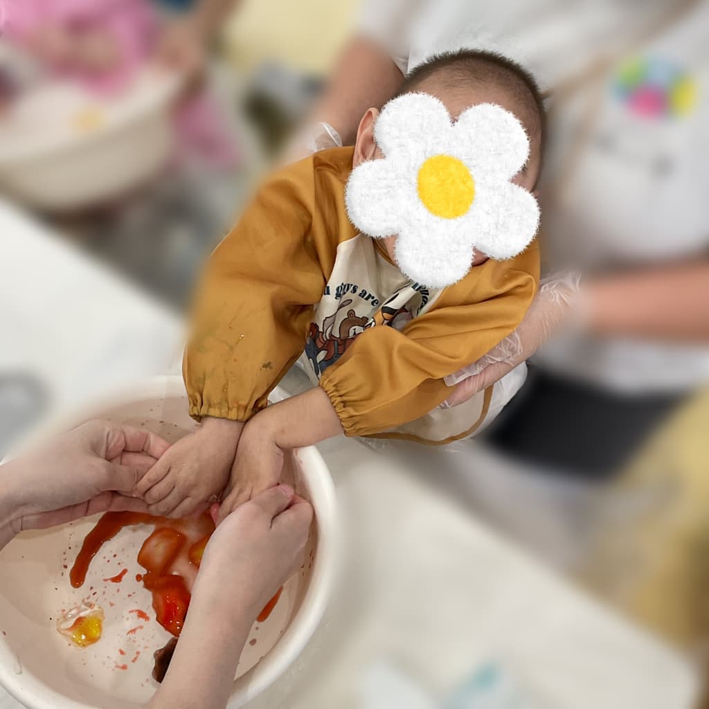 室内でスタッフに身体を支えてもらいながら、絵の具に両手で触れて感触を楽しむ子ども