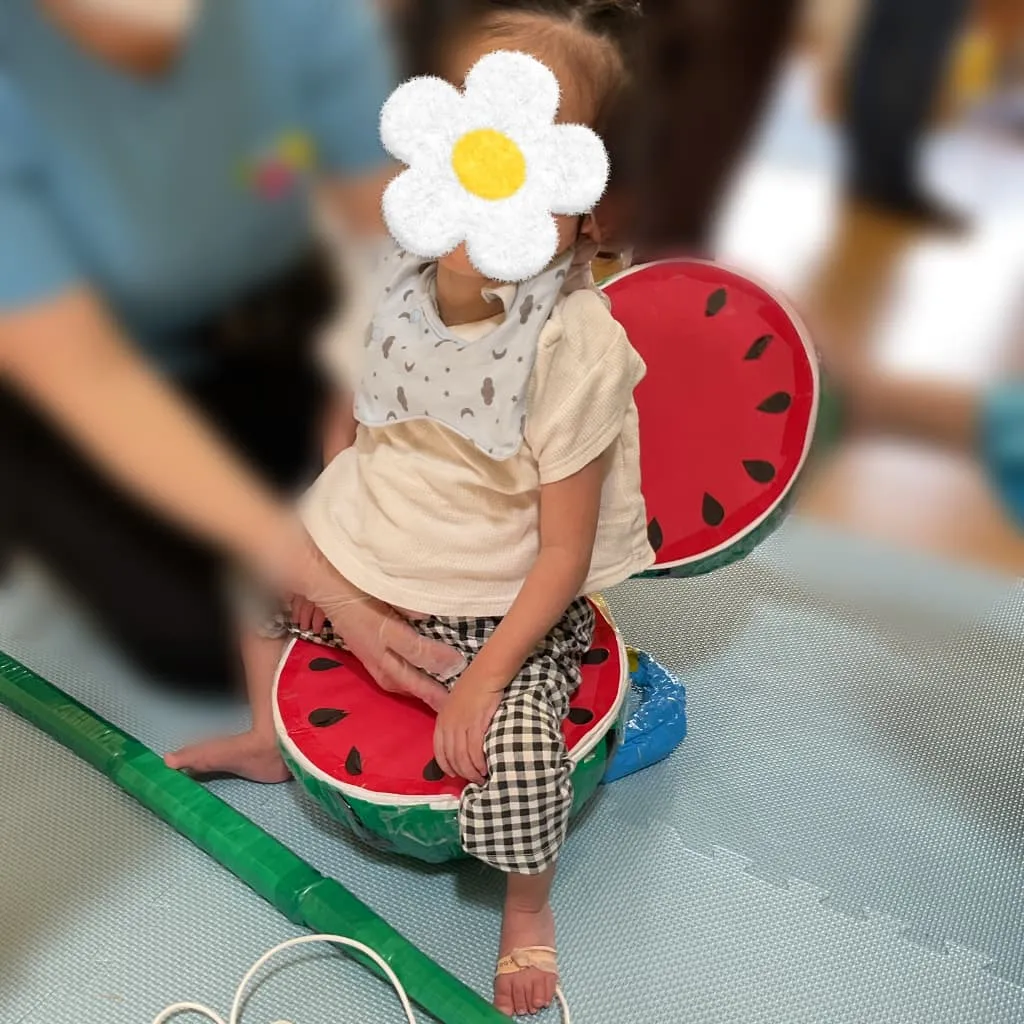 室内でスイカを模した椅子に座り、スイカ割りを楽しむ子ども