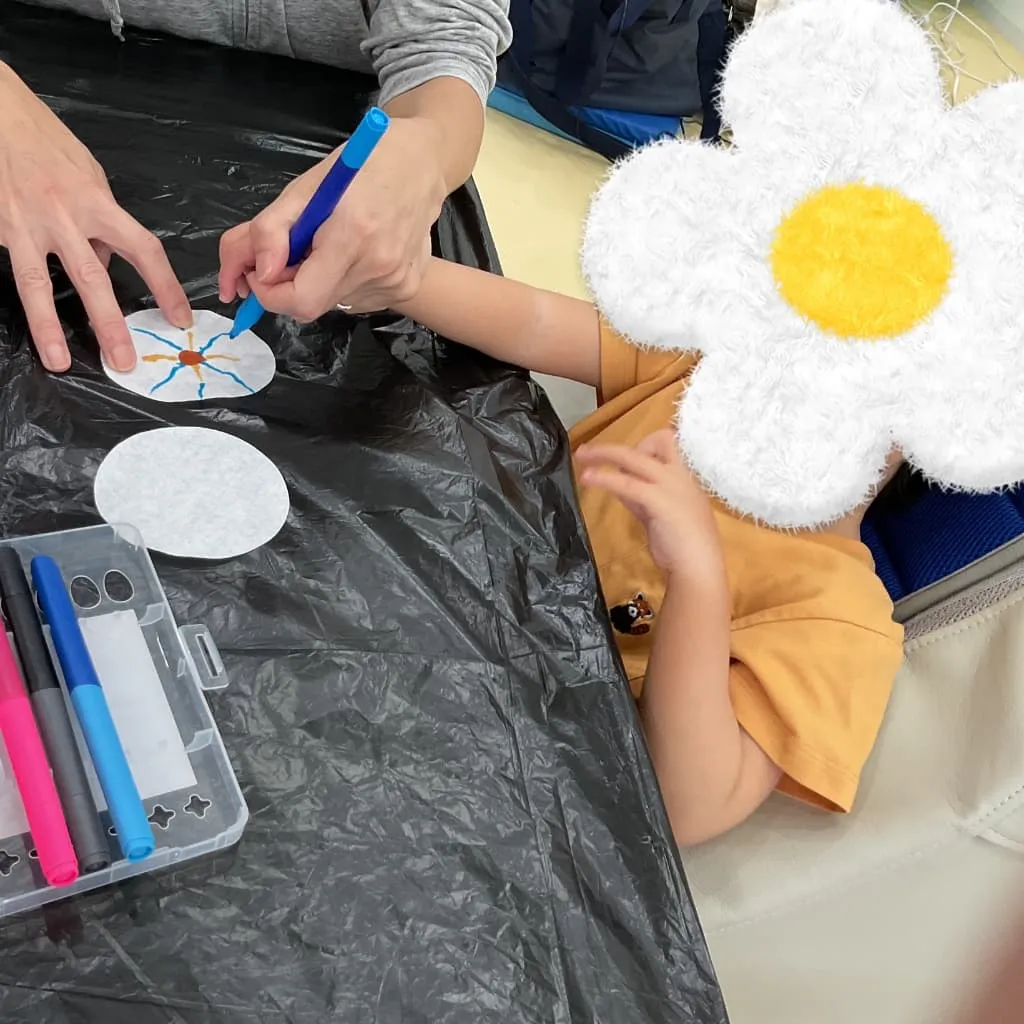 室内のテーブルでスタッフに手を支えてもらいながら、ペンで紙に模様を描く子ども