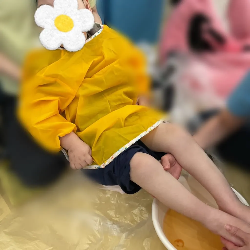 室内でスタッフに身体を支えてもらいながら、足を色水につける子ども