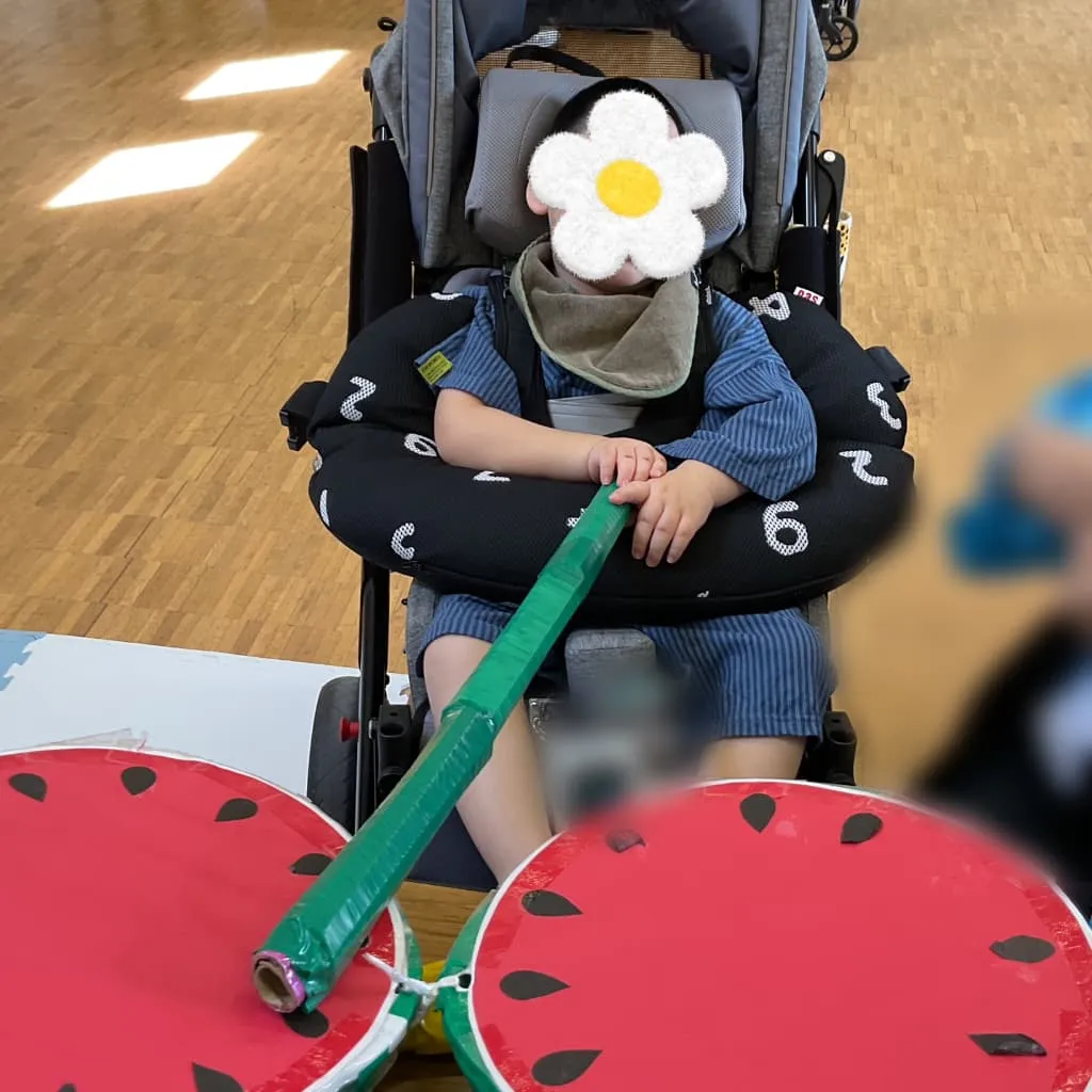 室内で車椅子に座り、緑色の棒を持ってスイカ割りに参加する子ども